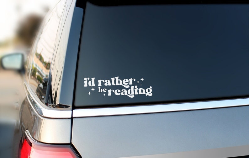 May include: A white vinyl sticker on a grey car that says "i'd rather be reading" with stars around the text.