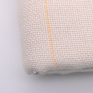 May include: Close-up of a white fabric with yellow stripes. The fabric has a woven texture.