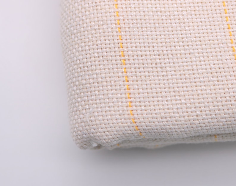 May include: Close-up of a white fabric with yellow stripes. The fabric has a woven texture.
