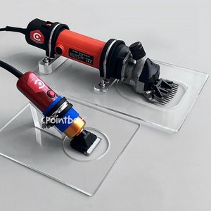 Könnte beinhalten: Zwei elektrische Tierhaarschneider auf klaren Acrylsockeln. Der größere Haarschneider ist rot und schwarz mit einem Kabel. Der kleinere Haarschneider ist rot, blau und gold mit einem Kabel. Beide Haarschneider haben ein C-Logo.