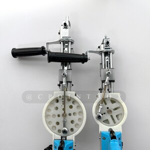 May include: Two silver and white tools with black handles and blue accents. The tools have a circular design with multiple holes and a lever on the side. The tools are mounted on a white surface. @CPOINTBOX