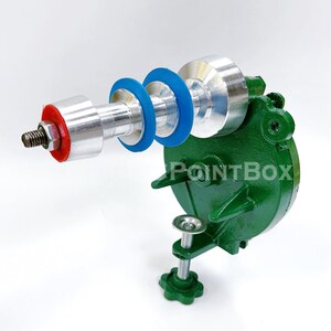 May include: A green metal tool with a silver and red handle and blue and red rings. The tool is mounted on a green base with a clamp.
