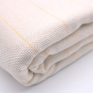 May include: A folded white throw blanket with thin yellow stripes. The blanket is made of a soft, woven fabric.