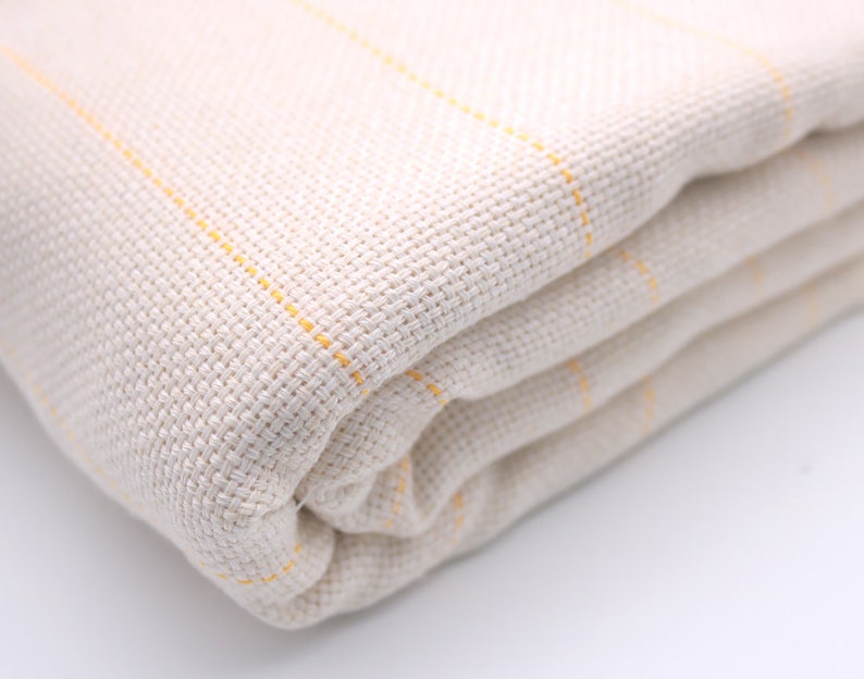 May include: A folded white throw blanket with thin yellow stripes. The blanket is made of a soft, woven fabric.