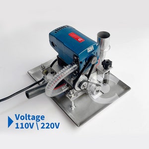 Puede incluir: Una lijadora eléctrica azul con una correa negra y una manguera transparente. La lijadora está sobre una base de metal plateado. La lijadora tiene un voltaje de 110V/220V.