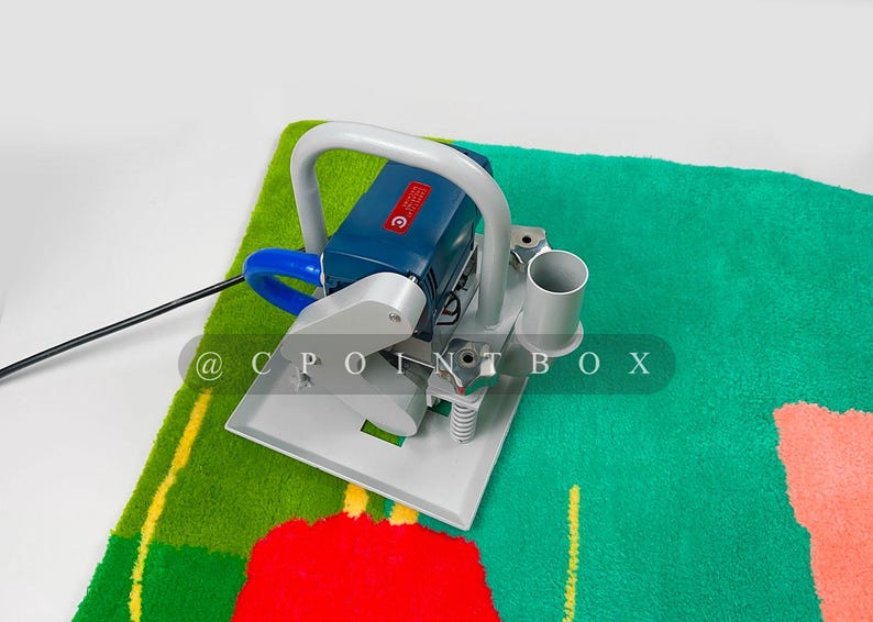 May include: A blue and gray electric carpet cleaning machine with a handle and a hose. The machine is on a green and red carpet with a yellow stripe.