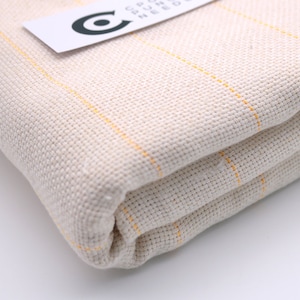 May include: A close-up of a folded piece of off-white fabric with thin yellow stripes. The fabric is woven and has a textured surface.