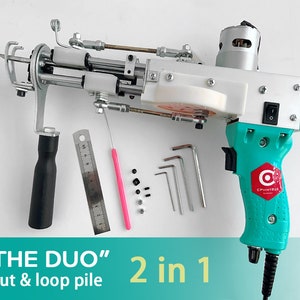 May include: A teal and white electric fabric cutting tool with a black cord and a red button. The tool is labeled "C POINT BOX" and has a black handle. The tool is on a white surface with a ruler, a pink tool, and small black and white pieces.