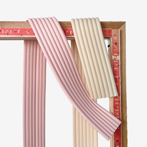 May include: Two strips of decorative trim, one pink and one cream, are attached to a wooden frame. The frame has red text that reads "CARPET" and "RIPPLE".