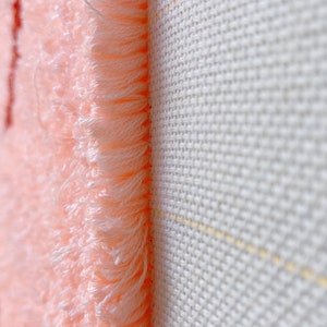 May include: Close-up of a pink fabric with a fuzzy texture, showing the edge of the fabric against a white background.