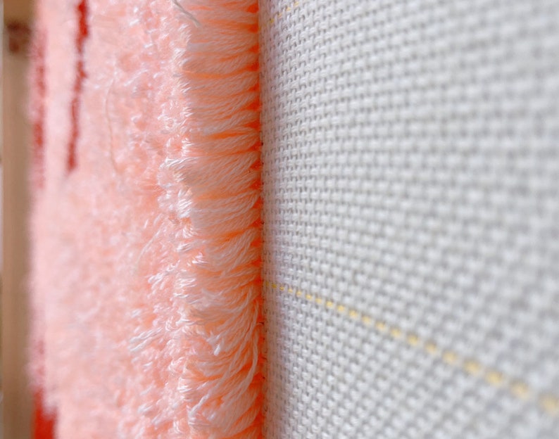 May include: Close-up of a pink fabric with a fuzzy texture, showing the edge of the fabric against a white background.