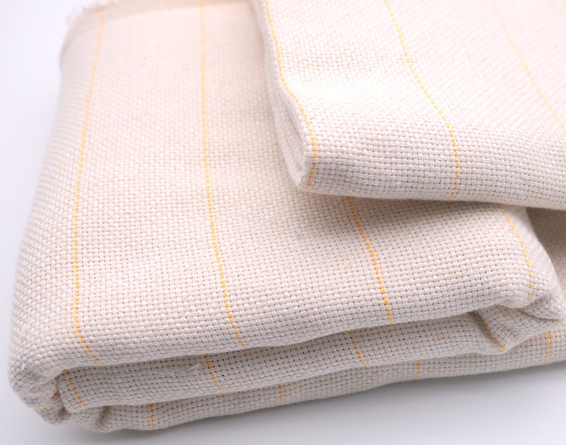 May include: A white fabric with thin yellow stripes folded in thirds. The fabric is woven and has a textured surface.