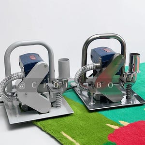 May include: Two gray and blue electric carpet tufting machines with handles and a clear hose. The machines are on a green and red patterned carpet.