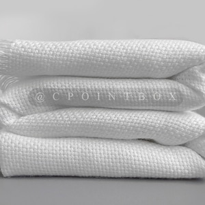 May include: Three white cotton blankets folded on top of each other. The blankets have a woven texture and a fringe edge.