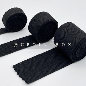 May include: Three black cotton twill ribbon rolls with a herringbone pattern. The ribbon is approximately 1 inch wide.