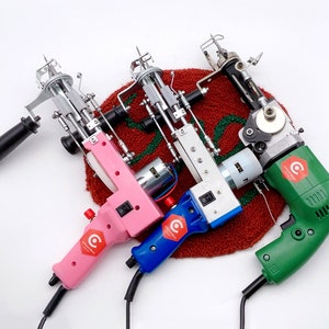 May include: Three electric fabric cutters with different colored handles: pink, blue, and green. The cutters are on a red and green rug. Each cutter has a small motor and a blade. The blades are visible in the image. The cutters are used for cutting fabric.