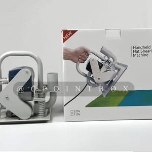 May include: A handheld flat shearing machine with a gray and silver body. The machine has a black cord and a clear hose. The machine is on a white surface. The box for the machine is white with the text "Handheld Flat Shearing Machine" and "NEW" printed on it. The box also has the text "120V" and "110V" printed on it.