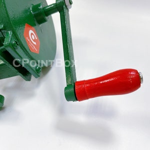 May include: Green metal hand crank food grinder with a red wooden handle. The grinder has a clamp to secure it to a surface. The handle has a metal end cap. The grinder has a CPOINTBOX logo.