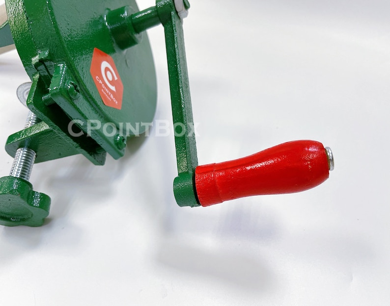 May include: Green metal hand crank food grinder with a red wooden handle. The grinder has a clamp to secure it to a surface. The handle has a metal end cap. The grinder has a CPOINTBOX logo.