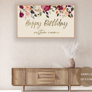 Puede incluir: Un letrero enmarcado con las palabras "Happy Birthday" en escritura dorada, con espacio para un nombre personalizado. La parte superior del letrero est&aacute; decorada con flores de acuarela en tonos rosa, burdeos y naranja.