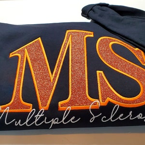 Pu&ograve; includere: Felpa con cappuccio blu navy con le lettere "MS" in glitter arancione, bordate di arancione, e le parole "Multiple Sclerosis" in corsivo bianco. Un nastro arancione di sensibilizzazione &egrave; sulla manica.