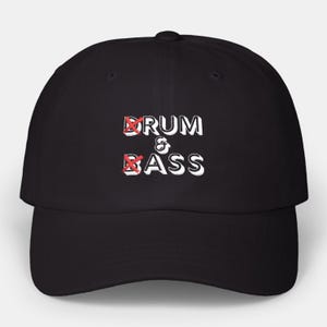 Op de afbeelding: Zwarte baseballcap met de witte tekst "DRUM & BASS", met rood doorgestreepte symbolen over de letters "D" en "B". De cap heeft een gebogen klep en een knoop aan de bovenkant.
