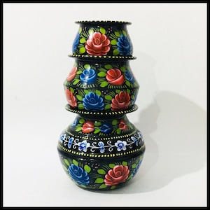 May include: A set of three black, hand-painted pots. Each pot features red and blue roses, green leaves, and white floral details. The pots are stacked, forming a decorative arrangement. The pots are likely made of metal.