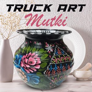 May include: A black ceramic pot, hand-painted with pink, blue, and green floral patterns. The pot has a wide opening and a rounded shape. The image includes the text "TRUCK ART" and "Mutki".