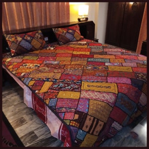 May include: A colourful patchwork quilt featuring a range of fabrics and textures. The quilt is composed of numerous squares and rectangles, each with a distinctive design. The quilt is a vibrant blend of colours, including red, orange, yellow, green, blue, and purple.