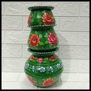May include: Three green, hand-painted ceramic pots stacked together. Each pot is decorated with red roses and green leaves. The bottom pot has white and blue floral accents.