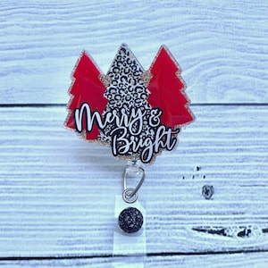 Op de afbeelding: Een rode en gouden glitter kerstboom badgehouder met de tekst "Merry & Bright".