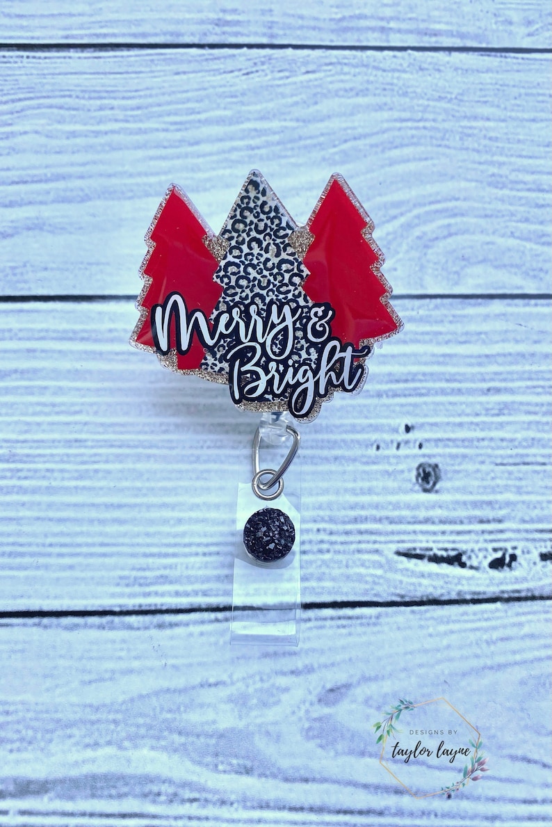 Op de afbeelding: Een rode en gouden glitter kerstboom badgehouder met de tekst "Merry & Bright".