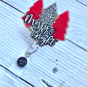 Op de afbeelding: Een rode en zwarte kerstboomvormige badgehouder met de tekst "Merry & Bright" in gouden glitter. De badgehouder heeft een zwarte glitterbedel bevestigd aan een transparante intrekbare badgehaspel.