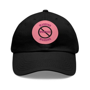 May include: Black baseball cap with a pink circle patch that says "WARRIOR" with a line through the word "WORRIER" in pink text.