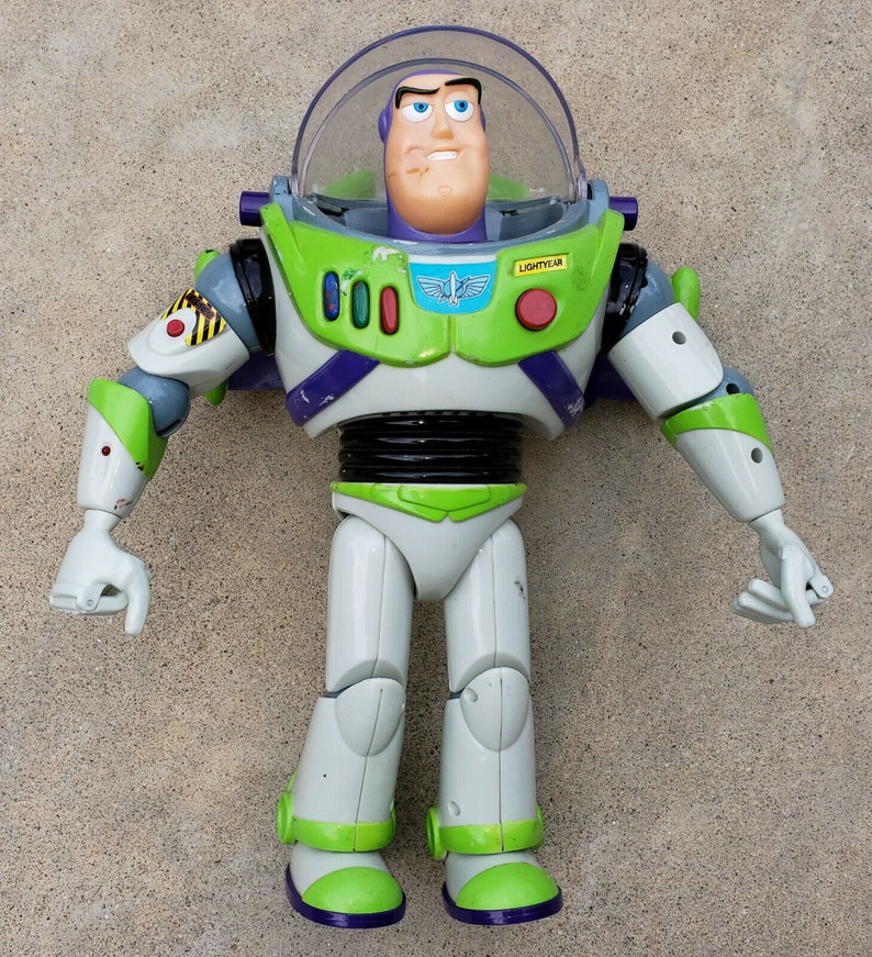 May include: A green and white plastic action figure of Buzz Lightyear from the Toy Story franchise. The figure has a purple chest piece with a red button that says "LIGHTYEAR".