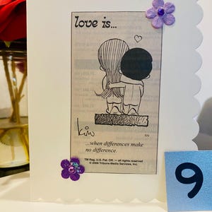 May include: A white card with a scalloped edge features a black and white cartoon illustration of a couple hugging. The text "love is..." and "...when differences make no difference." is printed on the card. The card is decorated with purple flowers and a blue number 9.