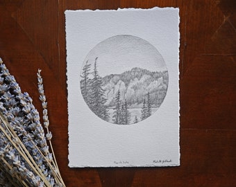 Könnte beinhalten: Eine Schwarzweiß-Bleistiftzeichnung eines Sees, umgeben von Bäumen und Bergen. Die Zeichnung ist in einem Kreis und ist signiert mit "Martis Lake" und "Madeline Jabloncki".