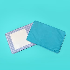 Könnte beinhalten: Zwei rechteckige Hundebettauflagen. Eine Auflage ist einfarbig türkis, die andere hat eine weiße Mitte, die von einem karierten Muster in Grau- und Weißtönen umgeben ist. Die Auflagen befinden sich auf einem türkisfarbenen Hintergrund.