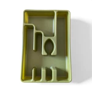 May include: Olive green plastic utensil organizer with multiple compartments. The organizer has a rectangular shape with various slots and sections designed to hold silverware and kitchen tools. The design includes a curved section for spoons and forks.