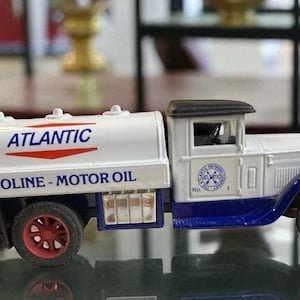 May include: A vintage toy Atlantic Gasoline and Motor Oil tanker truck. The white tank has the Atlantic logo and text. The truck is white with blue and black accents, and red wheels.