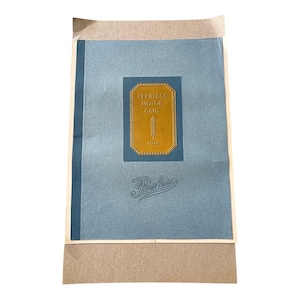May include: A vintage blue brochure for Peerless Motor Cars from 1912. The cover features a gold emblem with the text "Peerless Motor Cars 1912" and the Peerless logo in script. The brochure is in a tan paper sleeve.