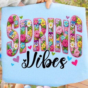 Puede incluir: Tela azul claro con las palabras "SPRING VIBES" en un dise&ntilde;o floral. Las letras est&aacute;n llenas de flores coloridas, incluyendo rosas, margaritas y pensamientos. Peque&ntilde;os corazones en rosa, verde y azul rodean el texto.