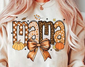 May include: Cream-colored sweatshirt with the word "MAMA" in a fall-themed design. The letters feature polka dots, leopard print, and autumn leaves. A large brown bow and pumpkins complete the design.