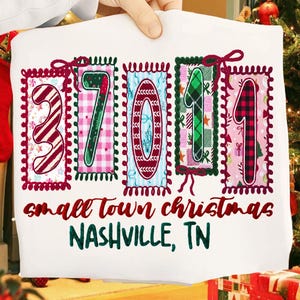 May include: White sweatshirt with a colorful Christmas-themed design. The design features the numbers "37011" in decorative frames, with the words "small town christmas" and "NASHVILLE, TN" in red and green text.