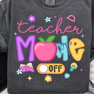 Puede incluir: Sudadera gris oscuro con las palabras "teacher Mode" en rosa, morado, azul y amarillo. El diseño incluye una manzana, flores, una regla, una bombilla y un libro abierto. La palabra "OFF" está debajo de la manzana.
