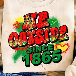 Puede incluir: Sudadera color crema con el texto "WE OUTSIDE SINCE 1865" en un diseño estilo grafiti. El texto es principalmente rojo con acentos amarillos, verdes y negros. El diseño incluye un corazón y una estrella.