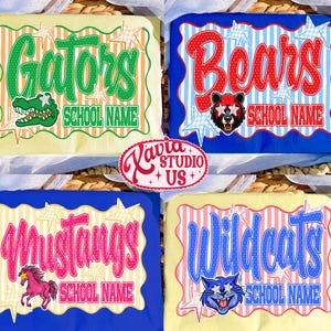 May include: Four t-shirts featuring school mascot designs. Top left: green Gators text with alligator graphic. Top right: red Bears text with bear graphic. Bottom left: pink Mustangs text with horse graphic. Bottom right: blue Wildcats text with cat graphic.