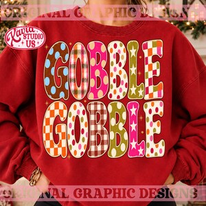 May include: A red crewneck sweatshirt featuring the text GOBBLE GOBBLE in large, multi-patterned letters. Each letter displays a unique design, including polka dots, plaid, gingham, and stars in vibrant colors like pink, orange, green, and brown.