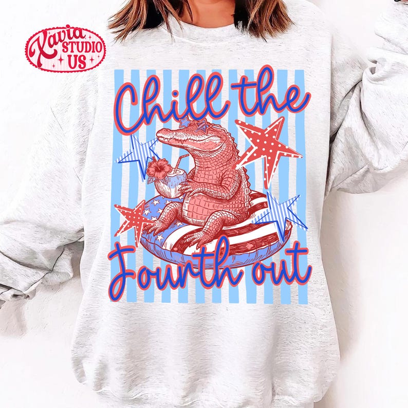May include: A light gray sweatshirt featuring a graphic of an alligator relaxing on an inflatable ring, holding a tropical drink. The design includes the text "Chill the Fourth out" in red and blue, with star accents.