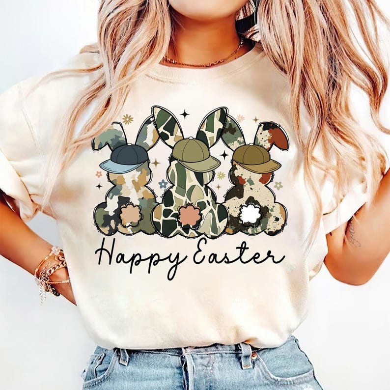 May include: A white t-shirt with a graphic of three camouflage Easter bunnies wearing baseball caps. The text "Happy Easter" is printed below the bunnies.